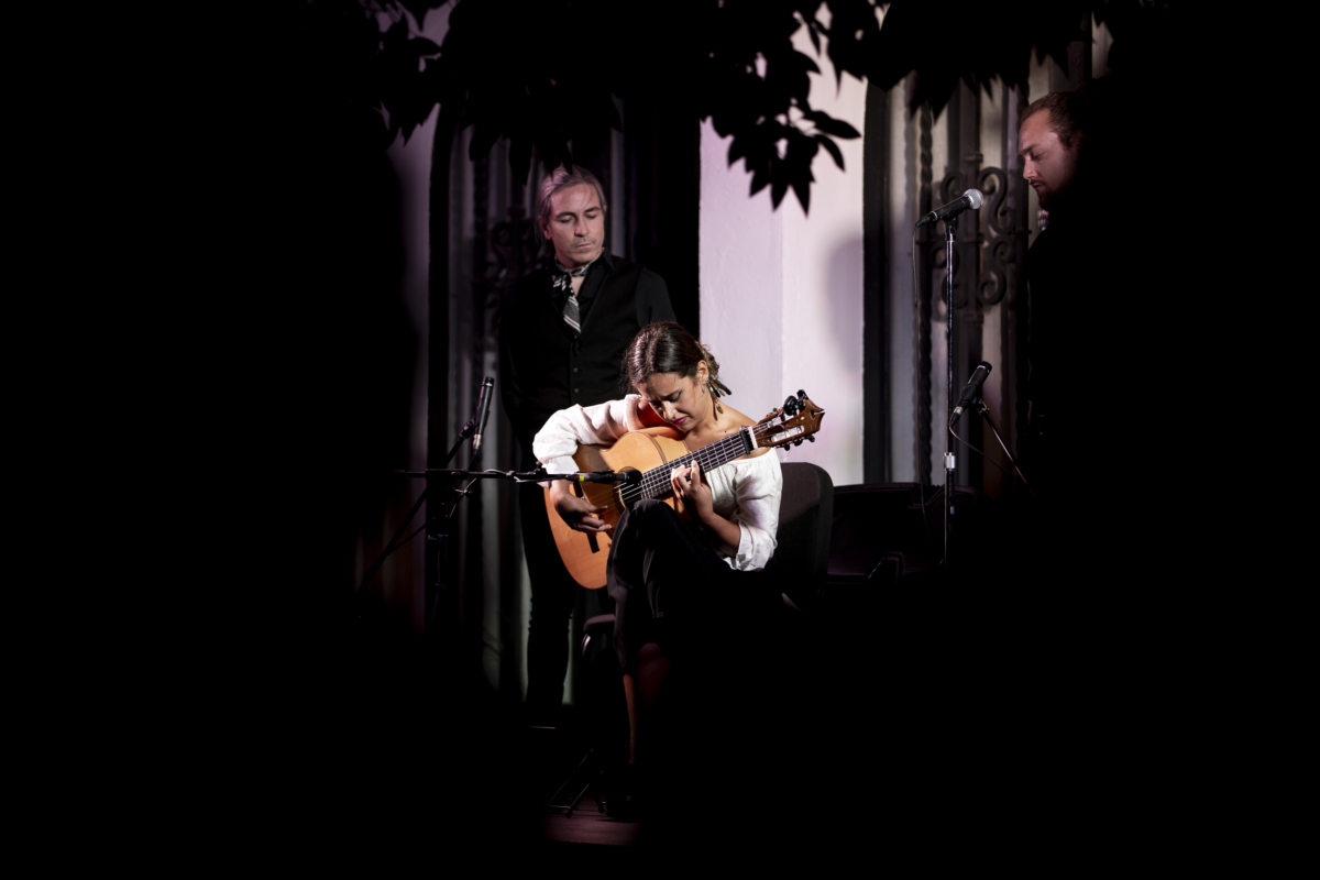 Una mujer tocando una guitarra mientras un hombre canta detrás de ella