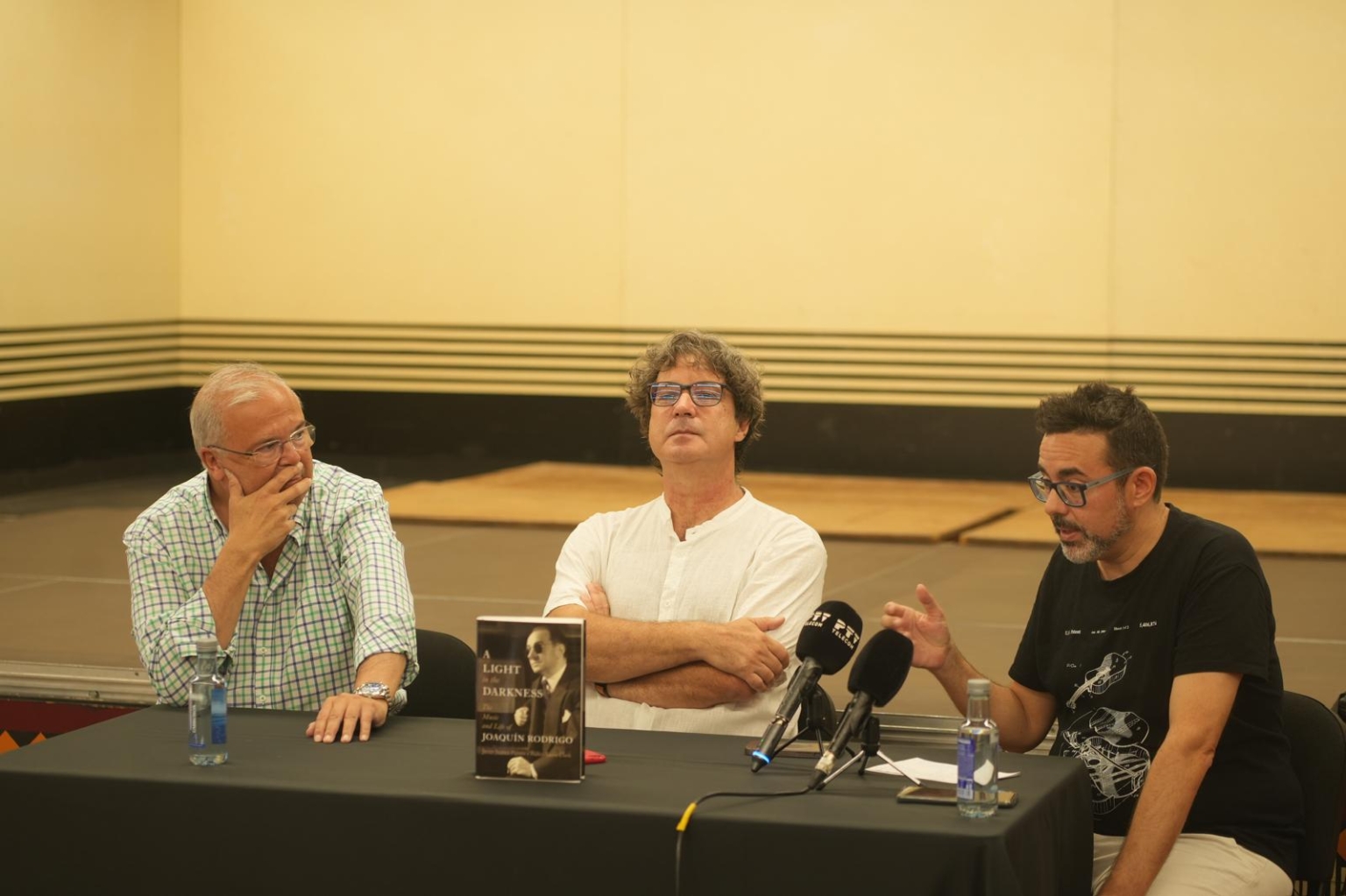 LIGHT 44 DARKNESS JOAQUIN RODRIGO. Tres hombres están sentados en una mesa con un libro que dice "poesía en español".