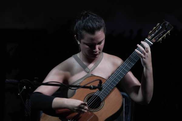 Una mujer toca una guitarra acústica en una habitación oscura